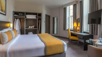 Una habitación de hotel con una cama, un escritorio, una silla, un televisor, un armario y una ventana.