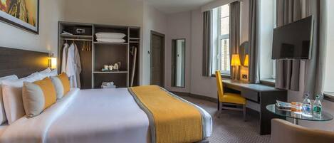 Una habitación de hotel con una cama, un escritorio, una silla, un televisor, un armario y una ventana.