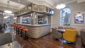 Un área de bar moderna con mostrador, taburetes y un espacio de estar con mesas y sillas.