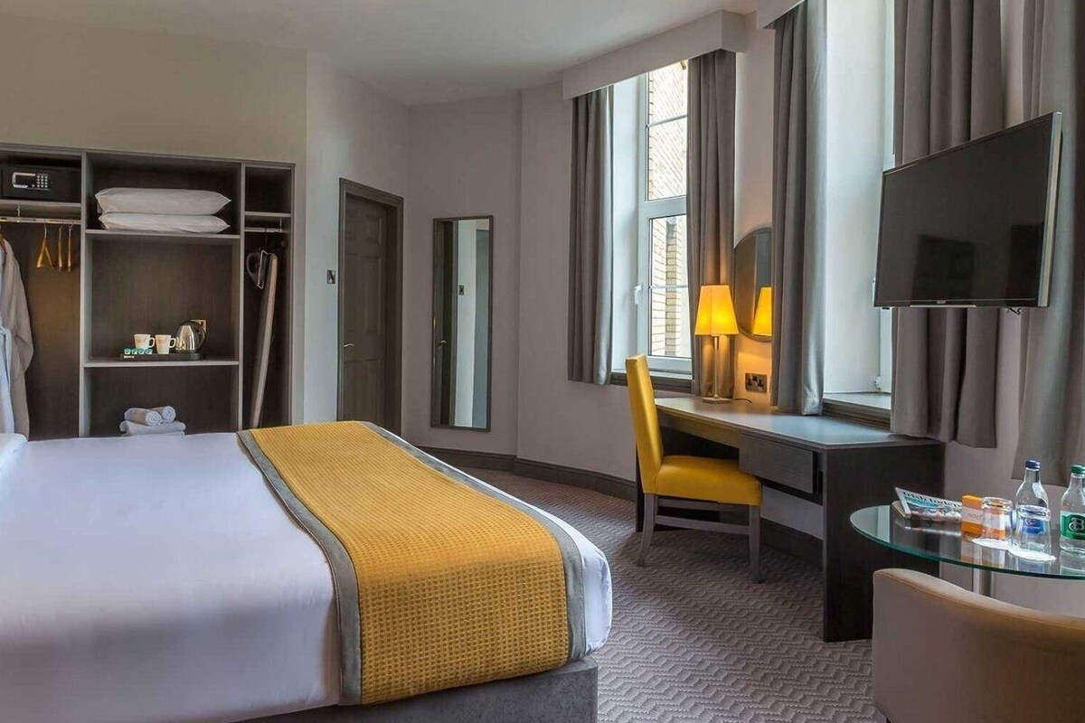 Una habitación de hotel con cama, escritorio, silla, televisor y armario.