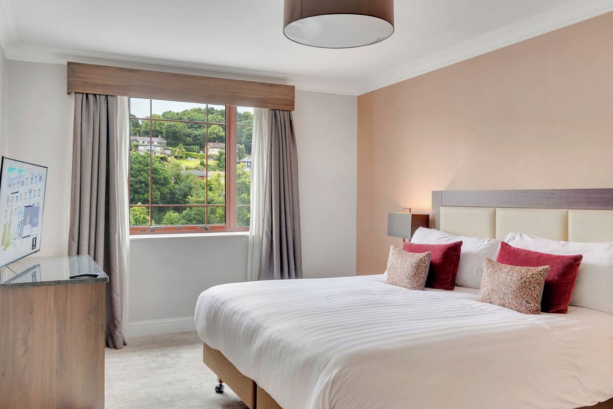A hotel room with a large bed, a desk, and a window with curtains.
