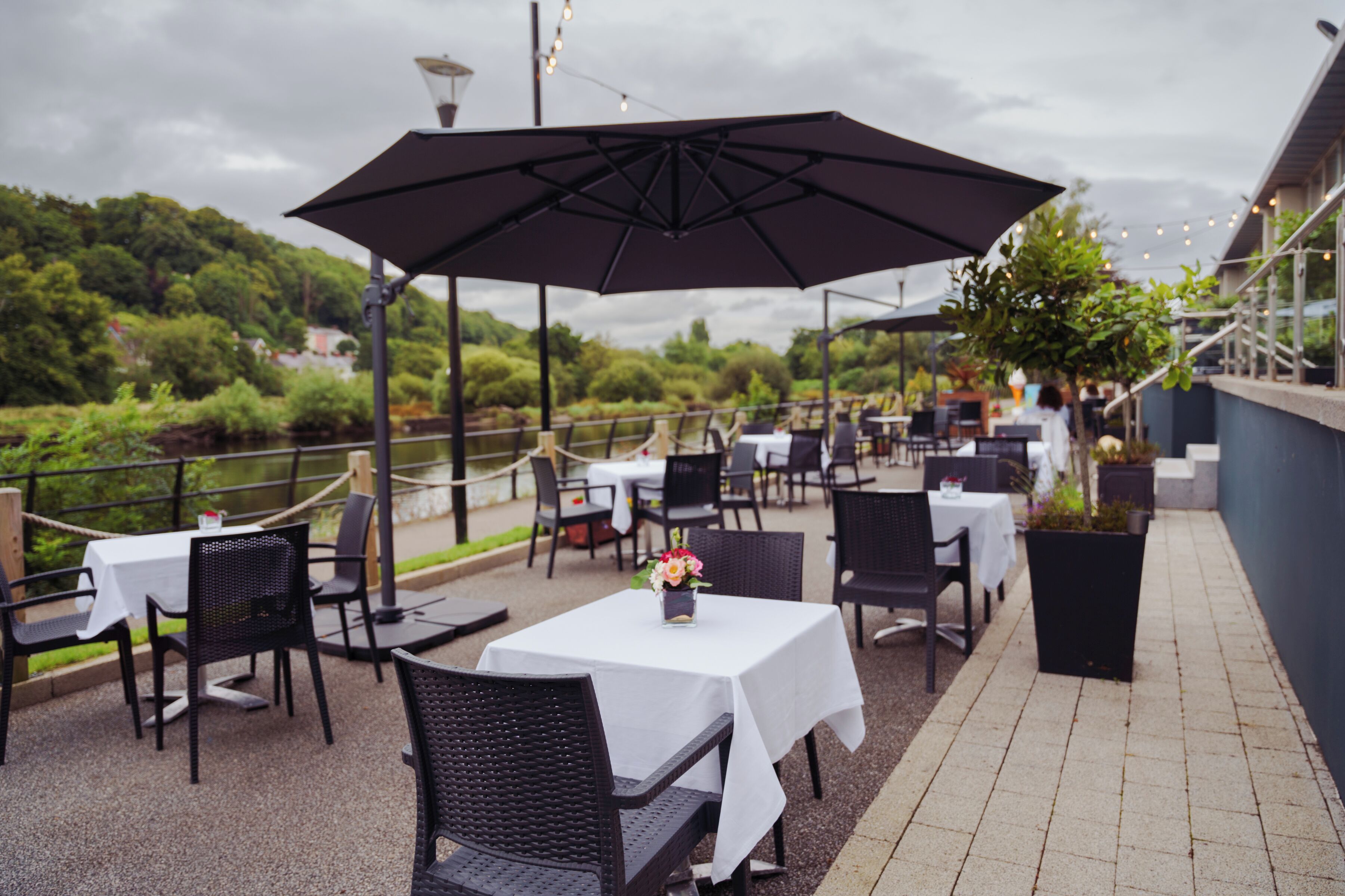 An outdoor patio with tables and chairs, umbrellas, and potted plants.
