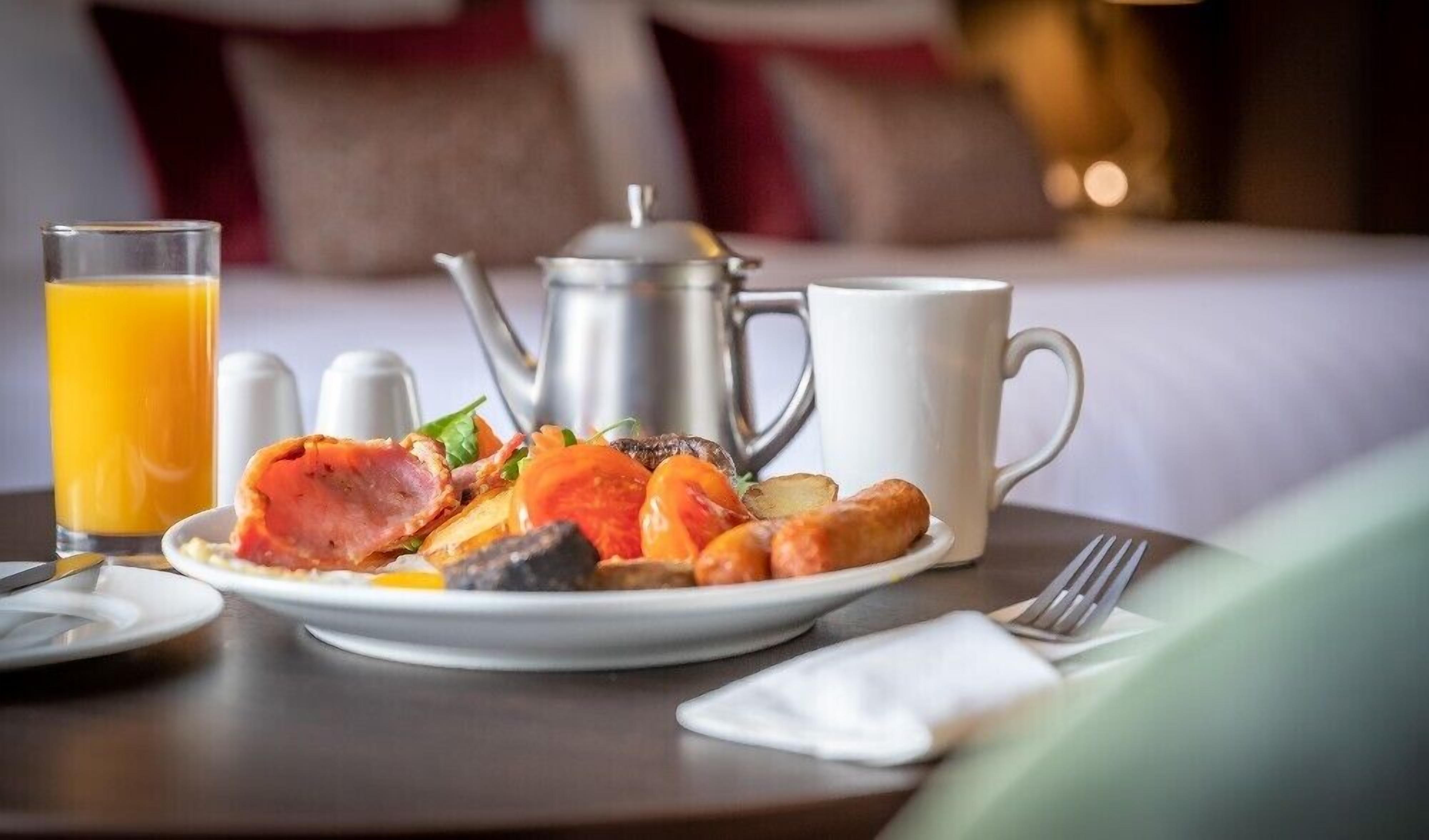 Une table mise pour le petit-déjeuner avec une assiette de nourriture, une théière, une tasse et un verre de jus d’orange.