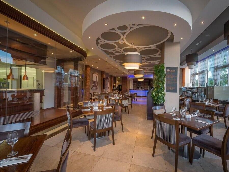 Un restaurante moderno con una zona de estar central, una barra a la izquierda y un ventanal grande a la derecha.