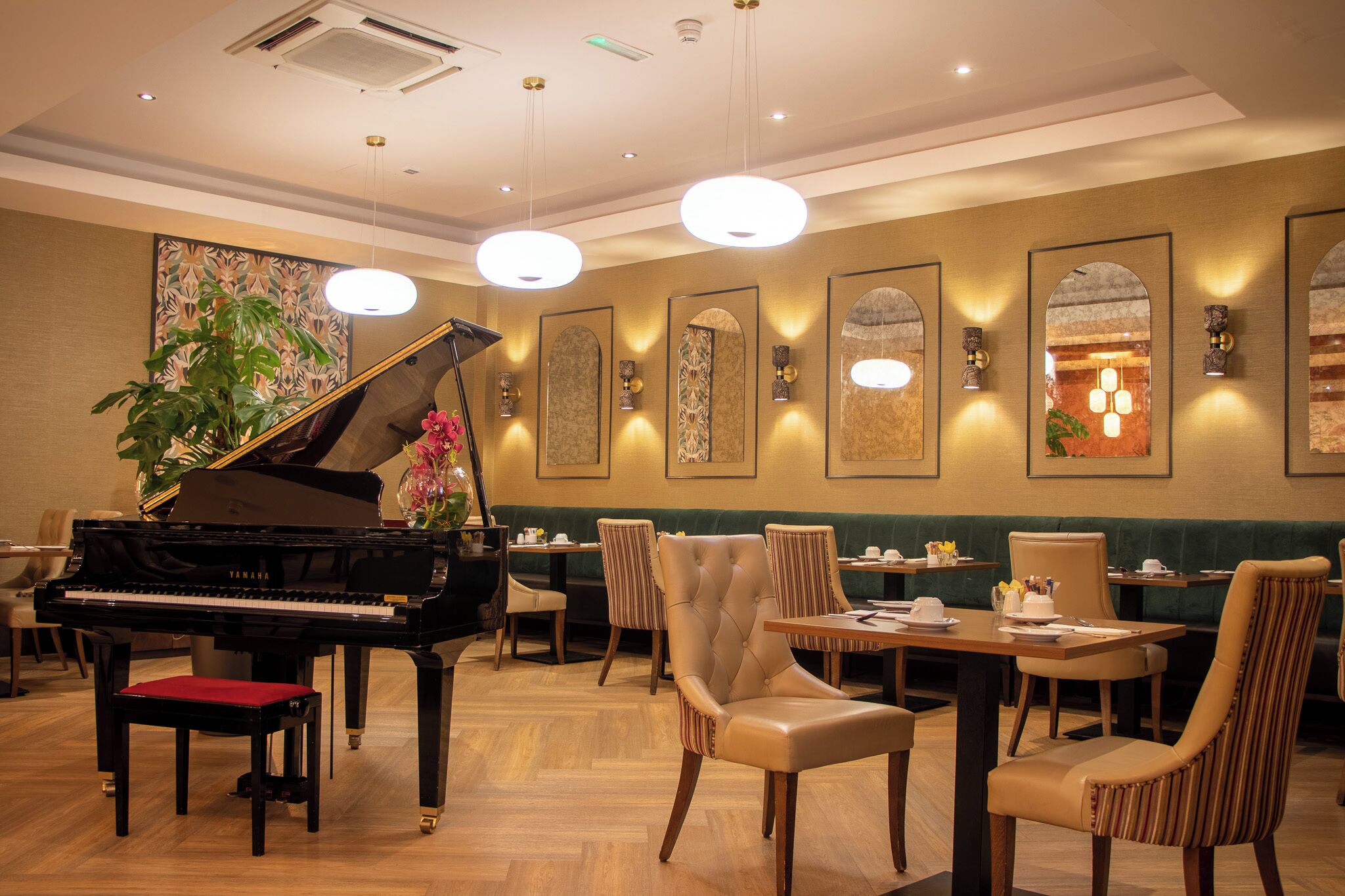 Um piano de cauda em uma sala ampla, com um banquinho estofado verde, mesas de jantar e cadeiras.