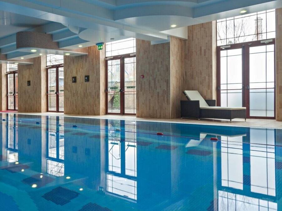Een groot binnenzwembad met helderblauw water, houten wanden en een modern plafond.