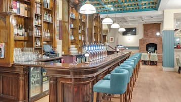 Zona de bar con estanterías de madera llenas de botellas, una barra larga con taburetes y una chimenea de ladrillo al fondo.