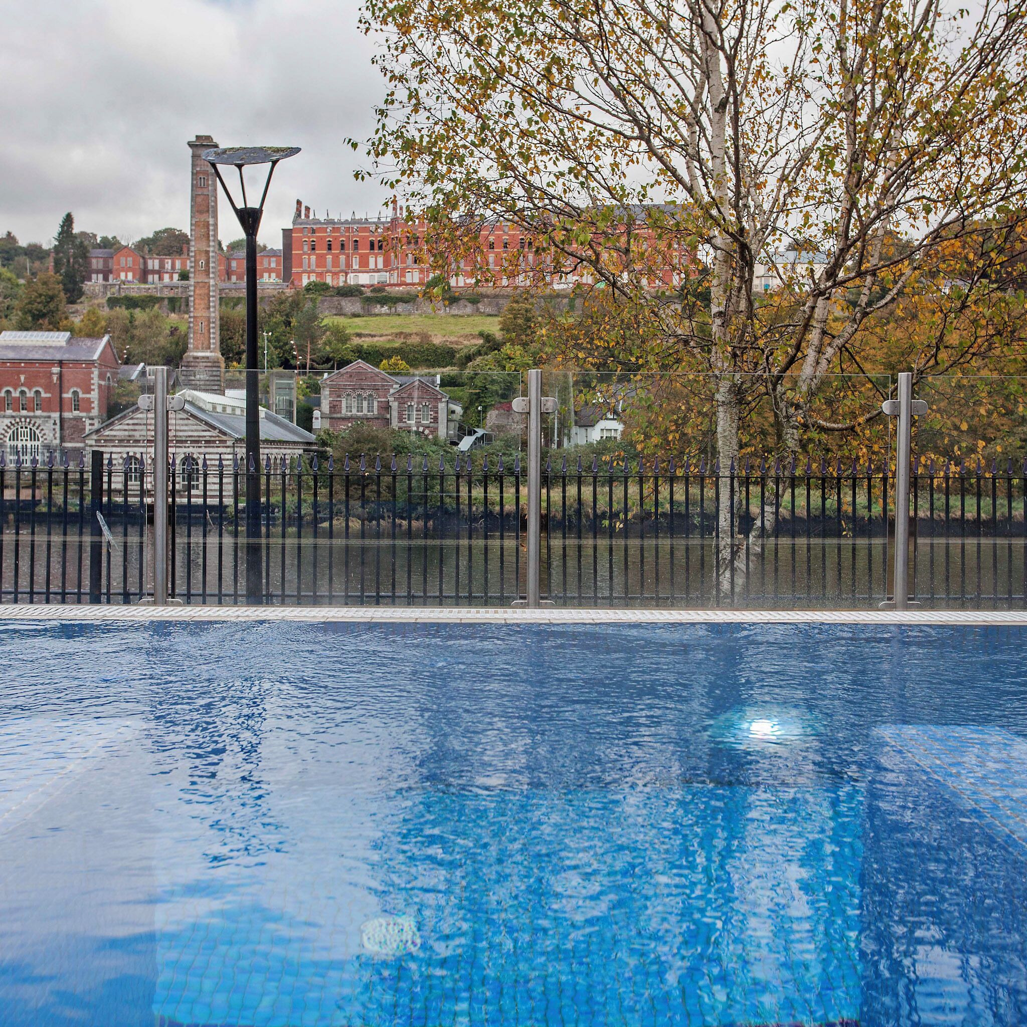 A swimming pool with a clear view of the surrounding area, including a building with a red facade and a tree with autumn leaves.
