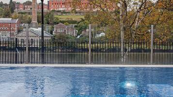 A swimming pool with a clear view of the surrounding area, including a building with a red facade and a tree with autumn leaves.