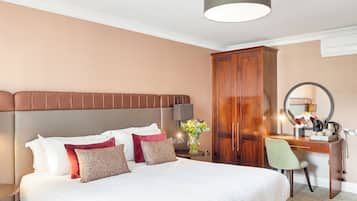 A hotel room with a large bed, a wooden wardrobe, a desk with a chair, and a mirror.