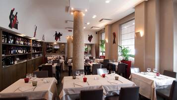 A restaurant with multiple tables set for dining, a wine bar with bottles, and decorative wall art.