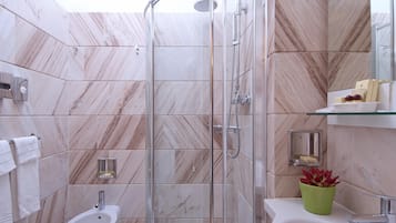 A modern bathroom with a glass-enclosed shower, a pedestal sink, and a glass shelf with toiletries.