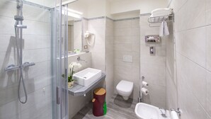 Een moderne badkamer met een douche met glazen wand, een wastafel, een toilet en een bidet.