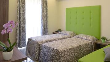 Habitación de hotel con dos camas, cabecero verde, escritorio con una planta y cortinas estampadas.