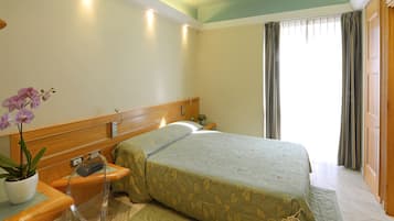 A hotel room with a bed, bedside table, lamp, and a potted orchid.