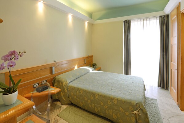 A hotel room with a bed, bedside table, lamp, and a potted orchid.