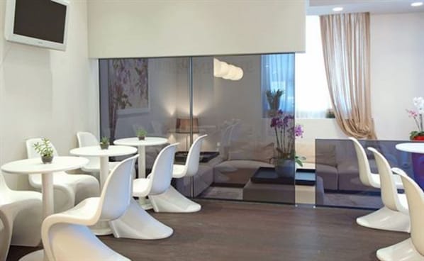 Una habitación de hotel moderna con muebles blancos, un ventanal con cortinas y vista a la ciudad.