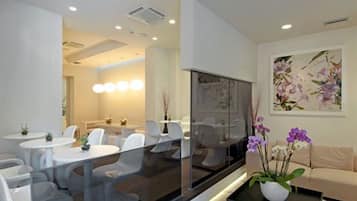 A modern hotel lobby with round tables, a sofa, and a large painting on the wall.
