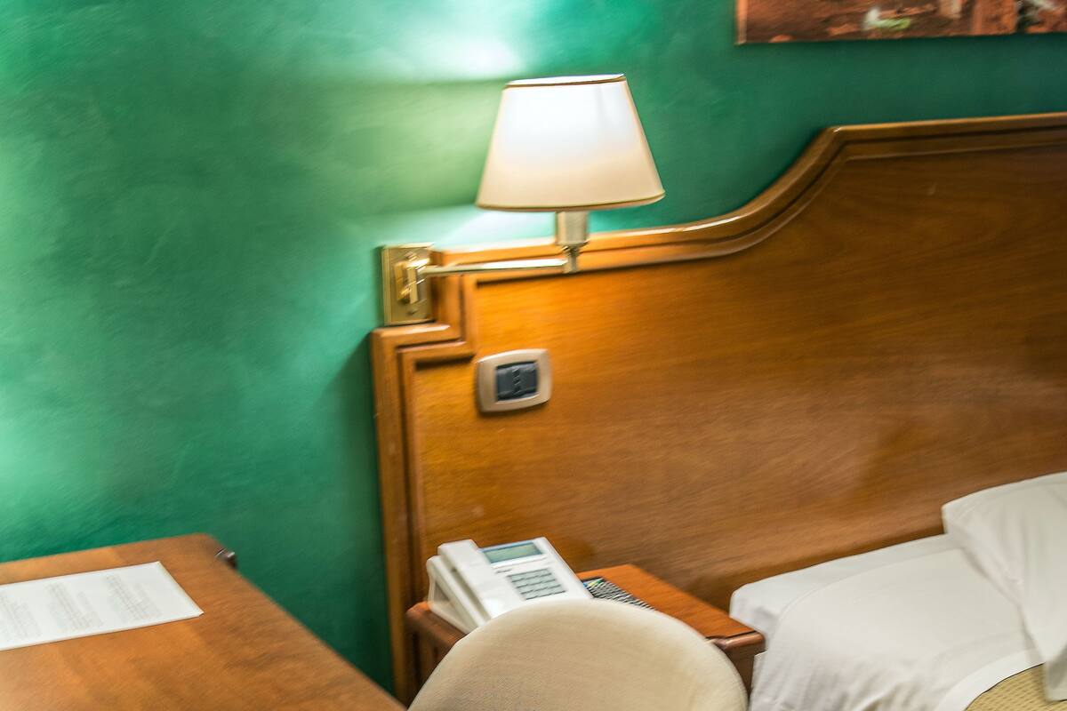 Una habitación de hotel con un escritorio de madera, un teléfono, una lámpara y una cama con cubrecama blanco.