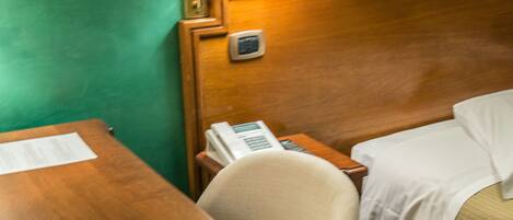 A hotel room with a wooden desk, a telephone, a lamp, and a bed with a white comforter.
