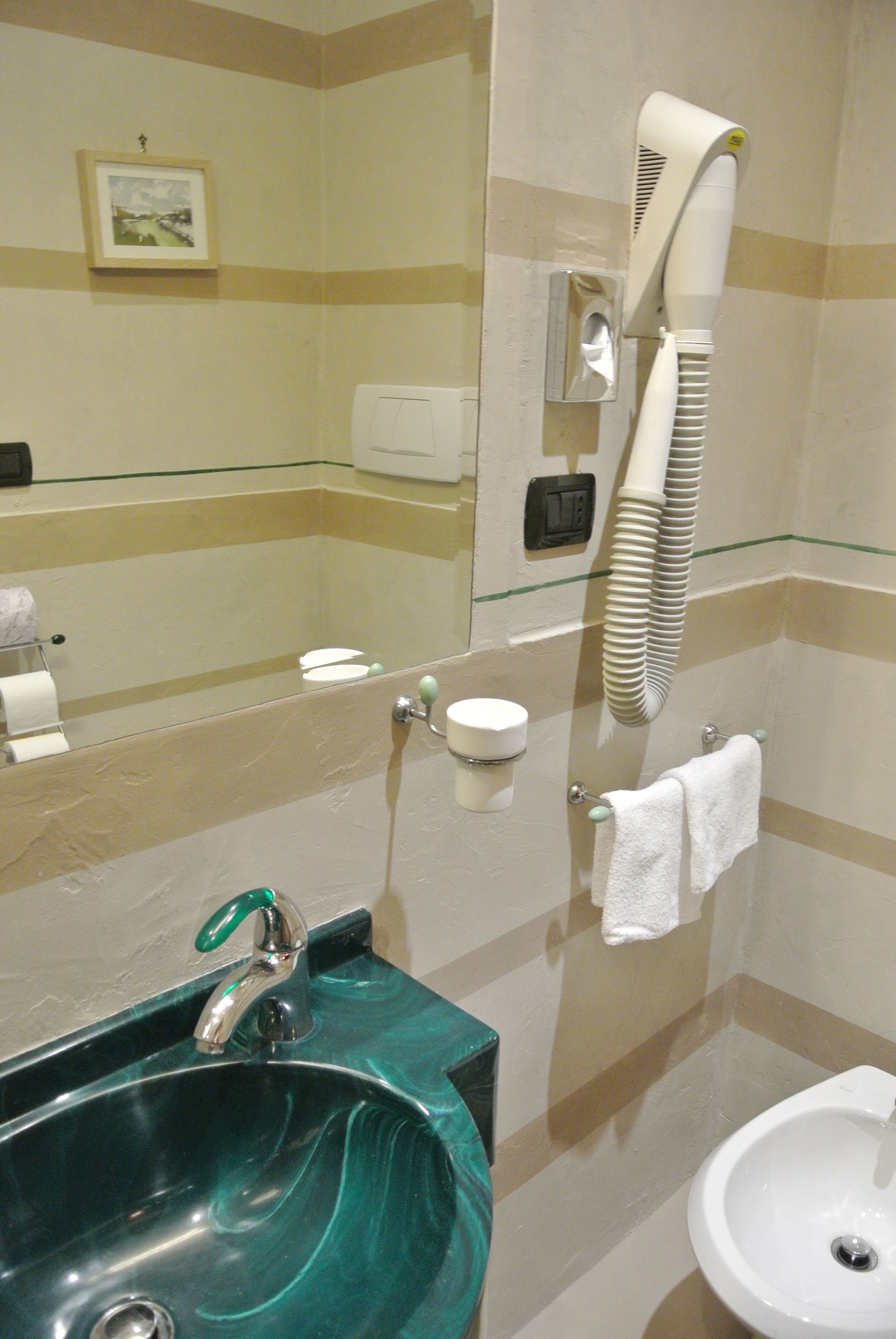 A bathroom with a green marble sink, a white pedestal sink, a hairdryer, and a towel rack.
