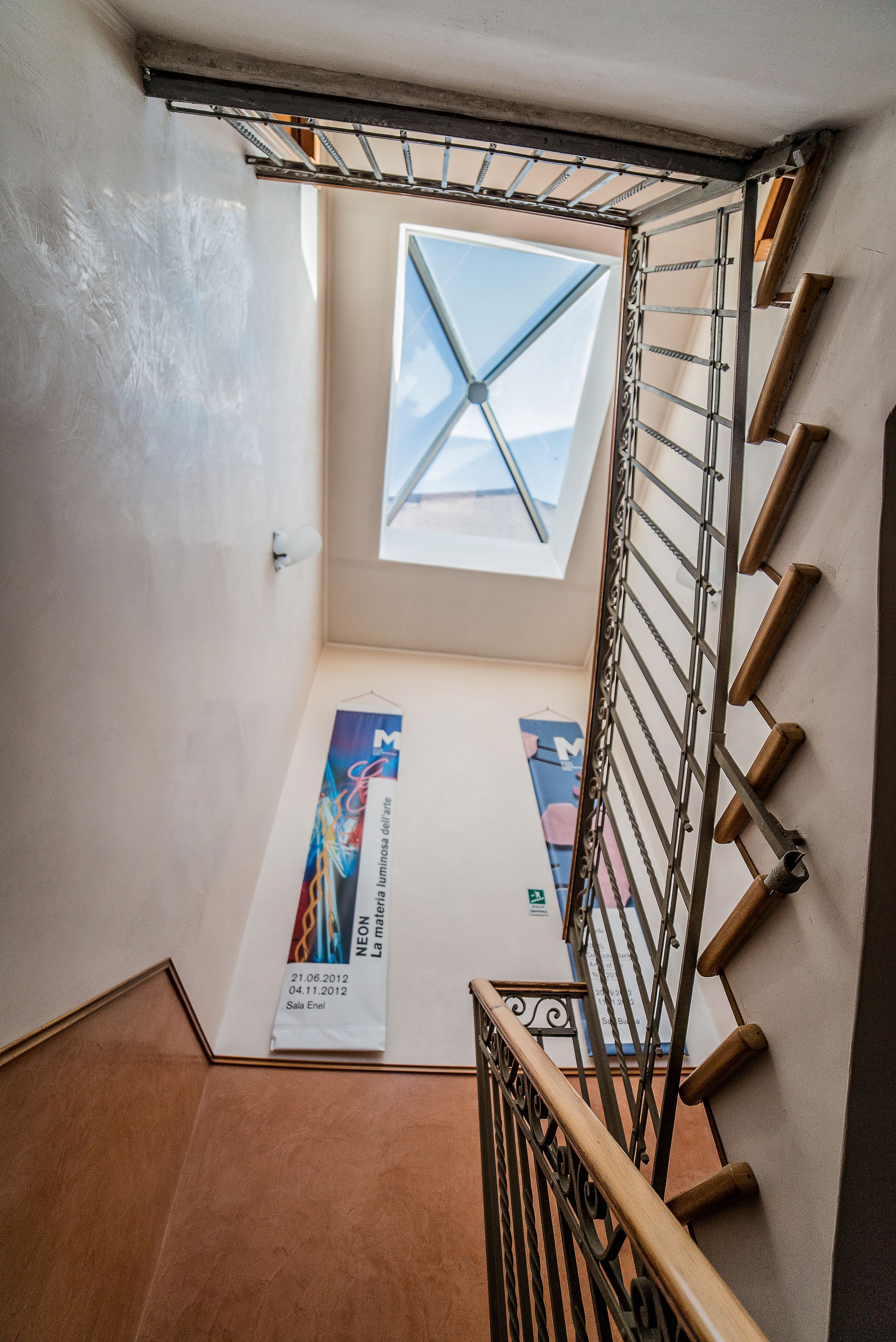 Un escalier avec une verrière, une main courante en métal et une affiche accrochée au mur.