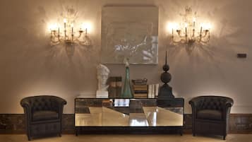 A lobby with a marble floor, a glass-top console table, two armchairs, wall sconces, and a bust sculpture.