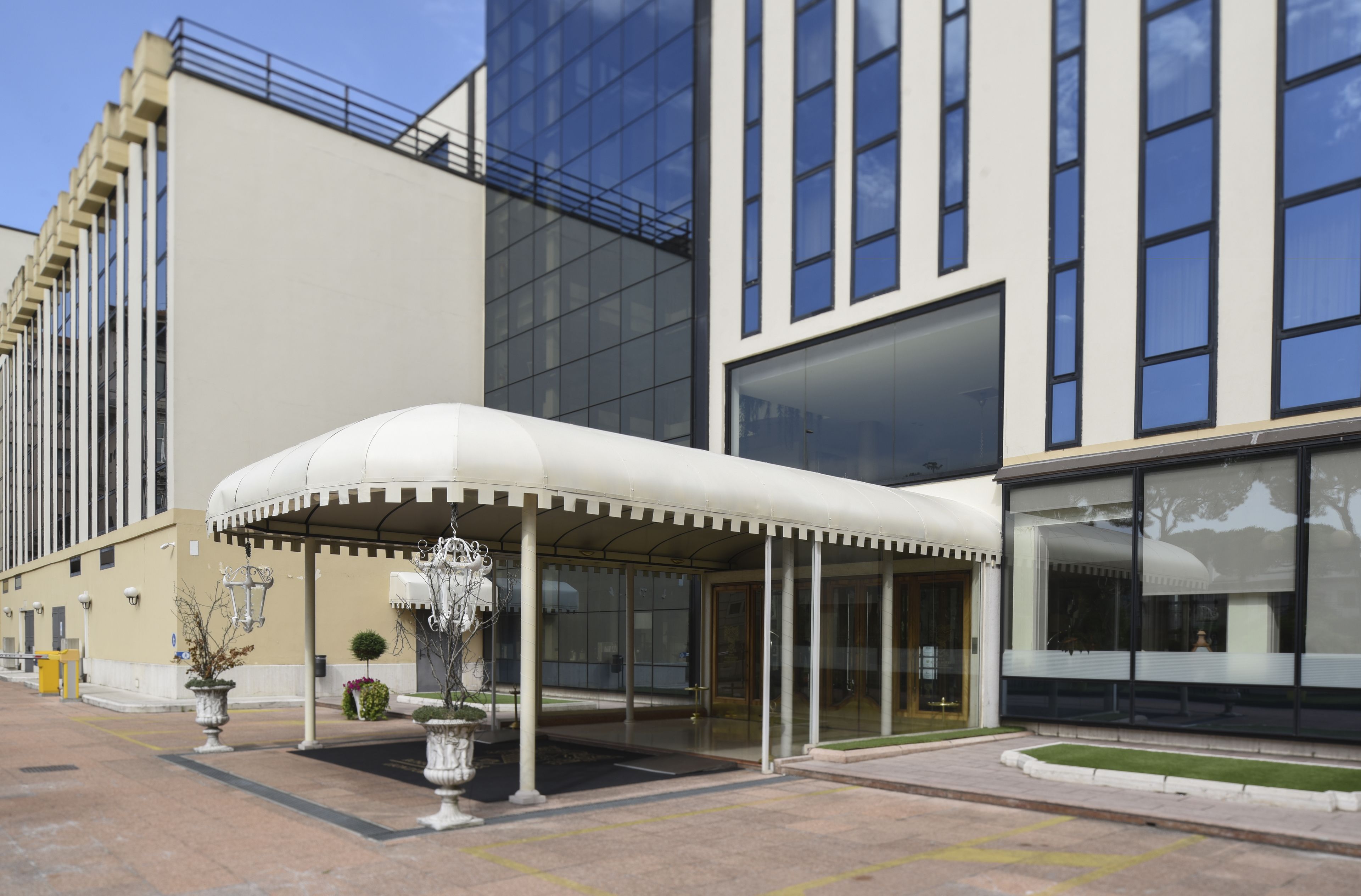Ein moderner Hotel Eingangsbereich mit überdachter Wartezone, großen Fenstern und einem gepflegten Außenbereich.