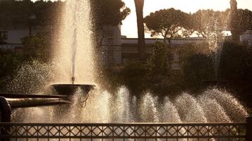 A fountain with water jets, surrounded by a fence, and trees in the background.