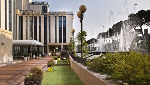 A courtyard with a fountain, green artificial turf, potted plants, and a modern building with large windows. - Hotel Leon d'Oro (Verona)