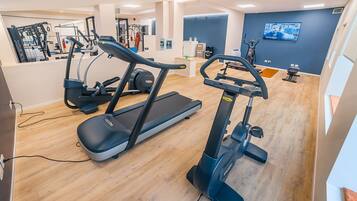 Una palestra moderna con macchinari cardio, attrezzature per sollevamento pesi e uno schermo televisivo.
