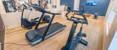 Uma academia moderna com máquinas de cardio, equipamentos de musculação e uma tela de televisão.