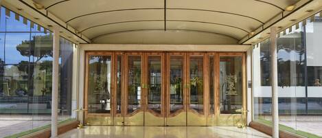 En hotels entré med en glasfacade, et overdækket område og et spejlende gulv.