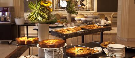 A buffet table with various cakes and pastries, a coffee machine, and a vase with flowers.