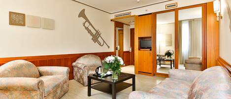 Habitación de hotel con sofá, una mesa de centro con flores, un trombón colgado en la pared y un televisor.