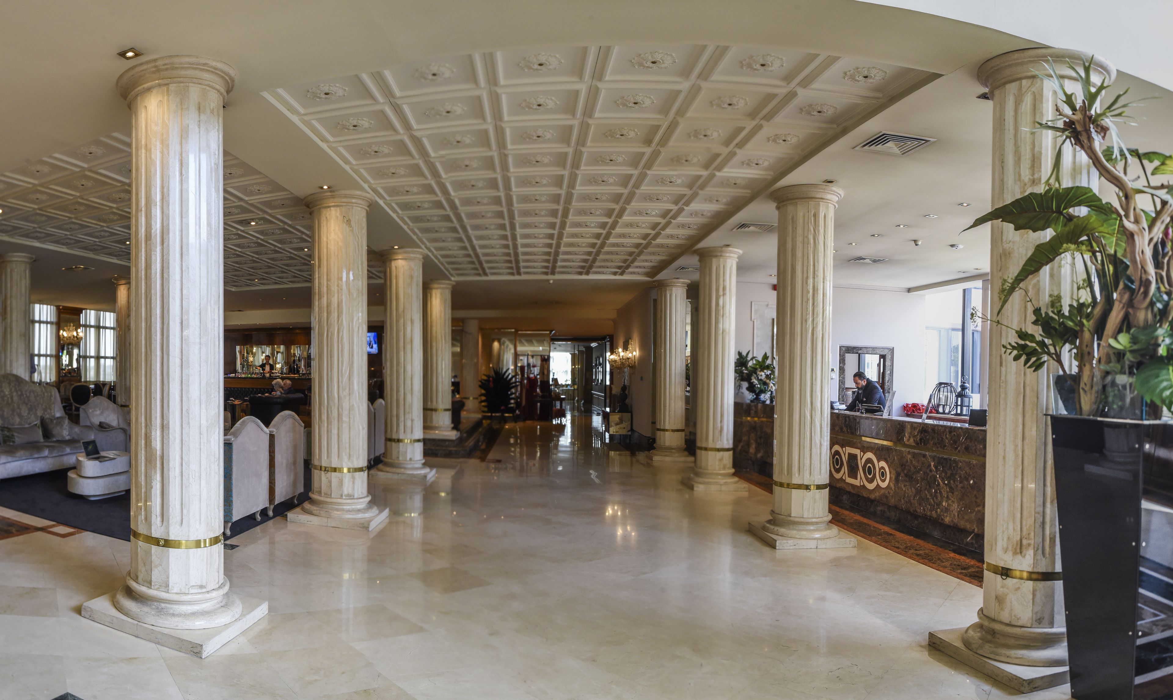 A grand lobby with marble columns, a polished floor, and a reception desk.