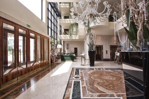 A spacious lobby with a marble floor, a grand chandelier, and a large wooden reception desk. - Hotel Leon d'Oro (Verona)