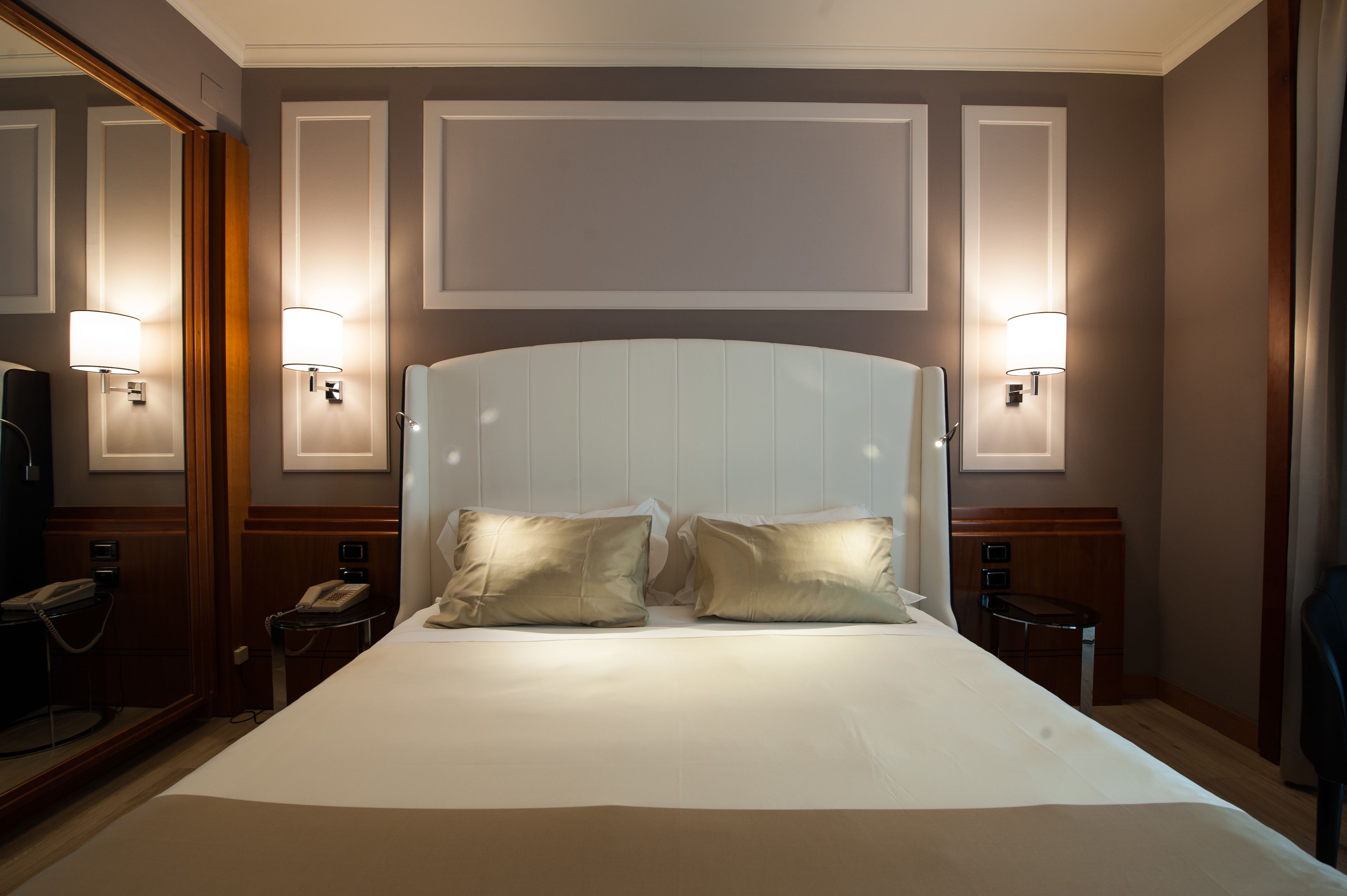 A hotel room with a large bed, two bedside lamps, a telephone, and a mirror.