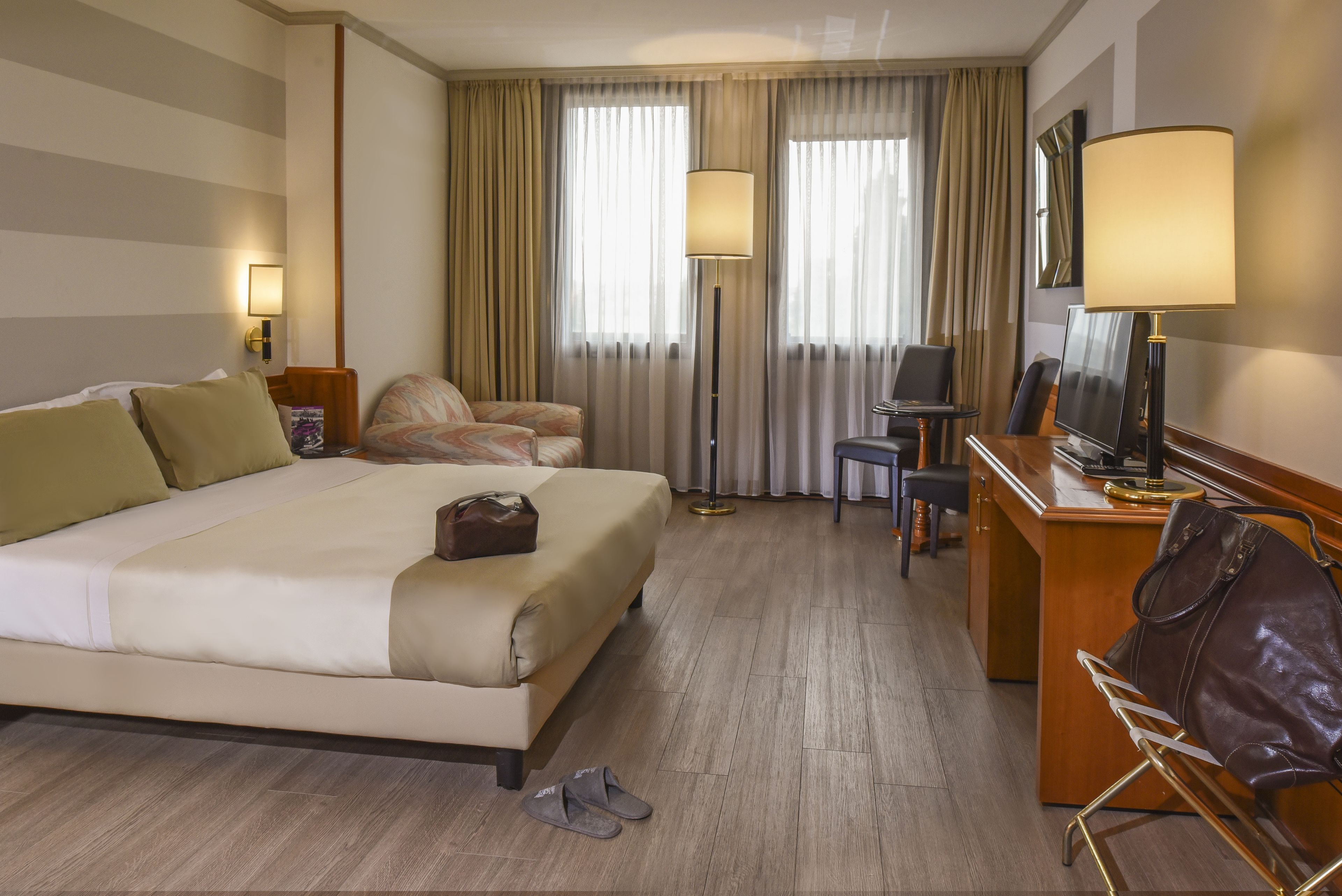 A hotel room with a large bed, a desk with a chair, a television, and a lamp.
