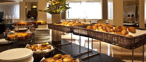 Una mesa de buffet con diversas pastas y postres, incluyendo croissants y pasteles, dispuestos en platos y cestas.