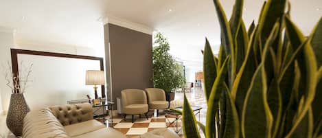 Una sala de estar moderna con un sofá, sillones, una lámpara y una planta grande.