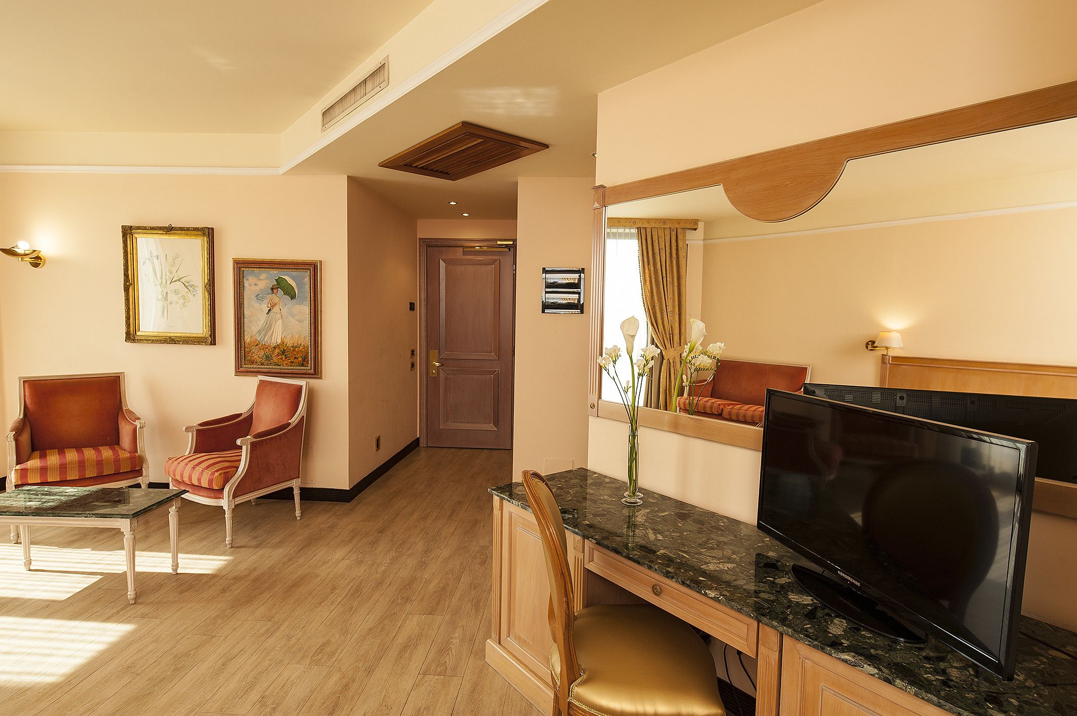 A hotel room with a TV, two armchairs, a coffee table, and a wooden desk.