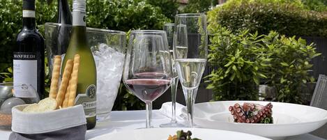 Una mesa al aire libre con comida, botellas de vino, copas y pan.