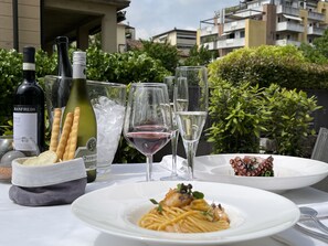 A table set outdoors with a meal, wine bottles, glasses, and bread.