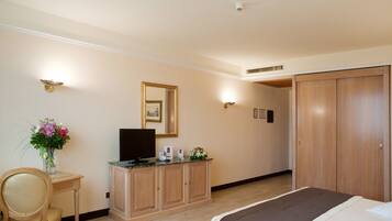 Une chambre d’hôtel comprenant un lit, une armoire en bois avec un téléviseur à écran plat, un bureau agrémenté d’un vase de fleurs et une penderie.