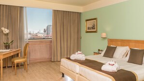 Ein Hotelzimmer mit Bett, Schreibtisch, Stuhl, einem Fenster mit Vorhängen, einer Lampe und einem Bild an der Wand.