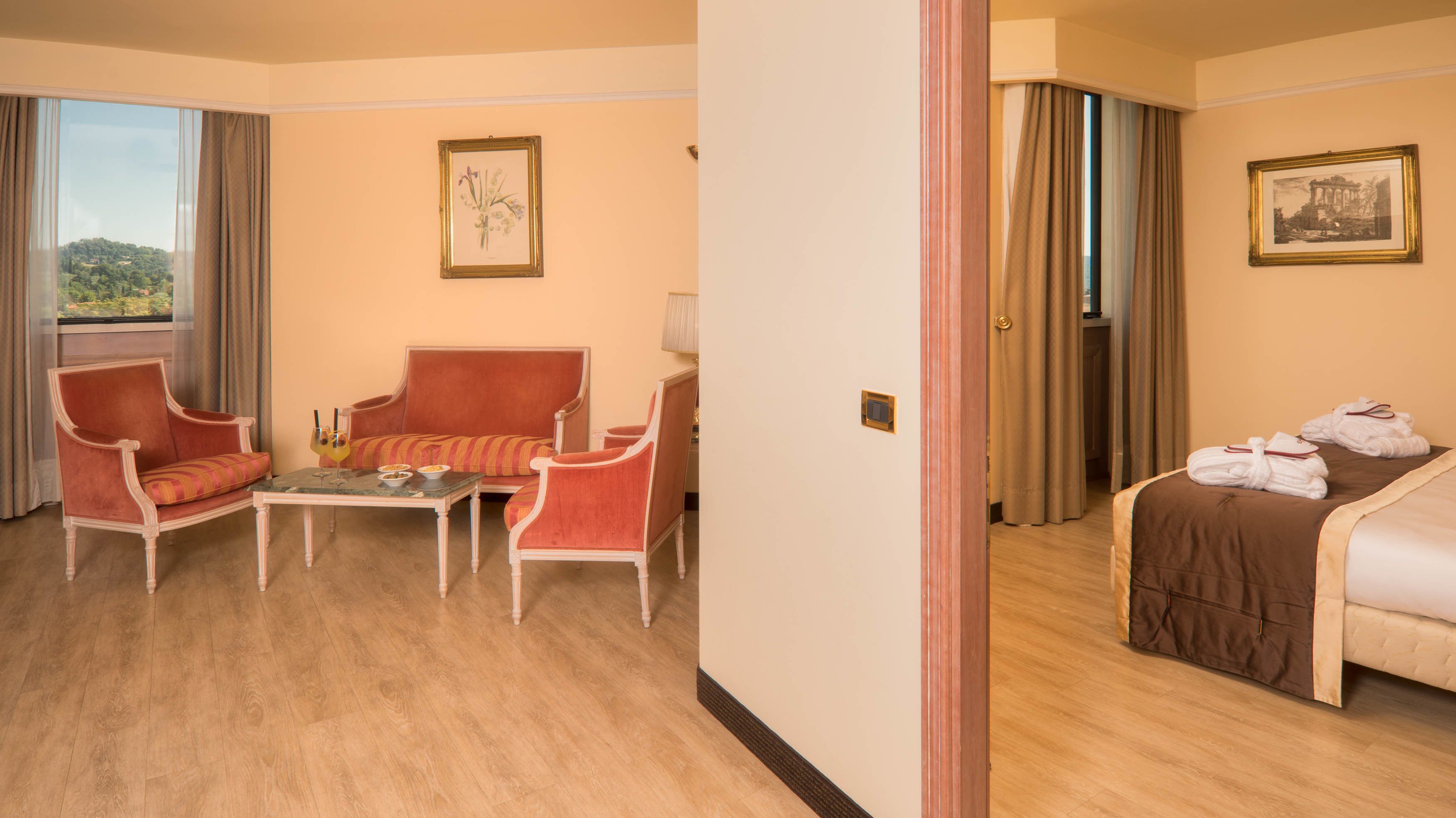 Habitación de hotel con sofá, sillones, una mesita, cama con toallas y dos cuadros en las paredes.