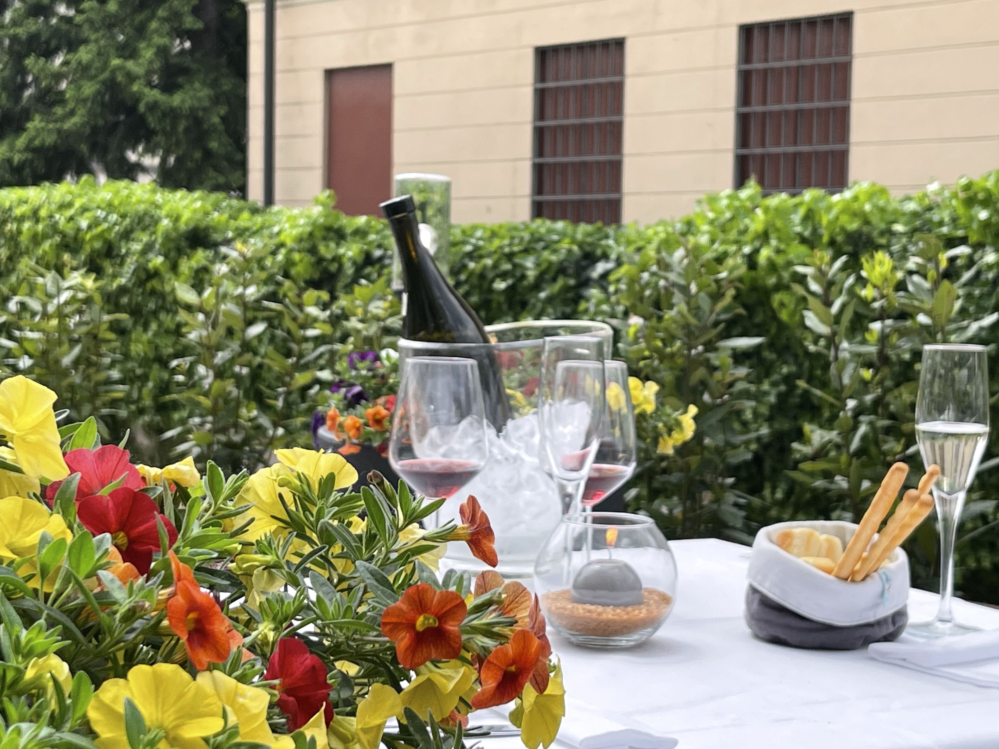 A table set outdoors with wine glasses, a bottle, and a bowl of breadsticks.