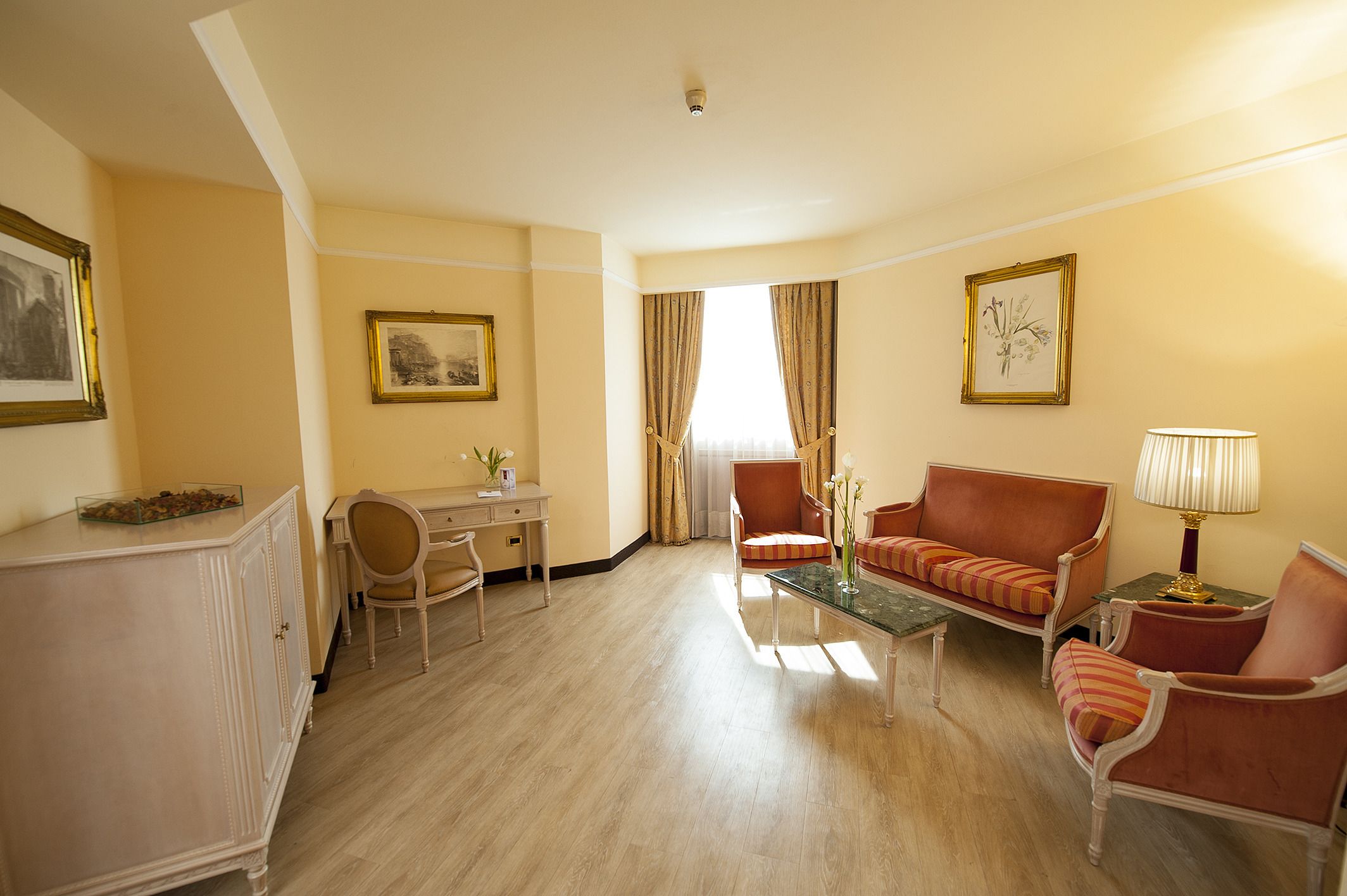 Ein Hotelzimmer mit Schreibtisch, zwei Sesseln, einem Sofa, einem Couchtisch und einer Lampe.
