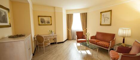 A hotel room with a desk, two armchairs, a sofa, a coffee table, and a lamp.
